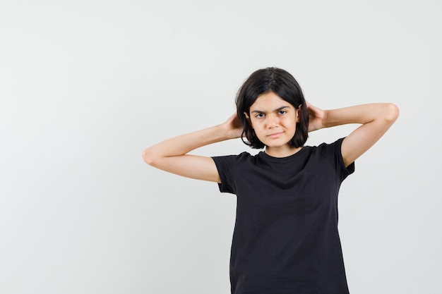 Niña cogidos de la mano detrás de la cabeza en camiseta negra y mirando confiada. vista frontal.