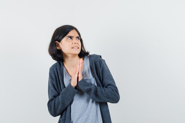 Niña cogidos de la mano en gesto de oración en camiseta, chaqueta y mirando asustado,