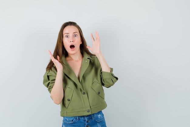 Niña cogidos de la mano levantados en chaqueta, pantalones cortos y mirando sorprendido, vista frontal.