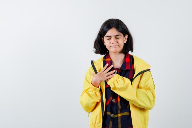 Niña cogidos de la mano en el pecho con camisa a cuadros, chaqueta y mirando esperanzado, vista frontal.