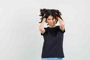 Foto gratuita niña cogidos de la mano en el pelo en camiseta negra, pantalones cortos y mirando angustiado, vista frontal.
