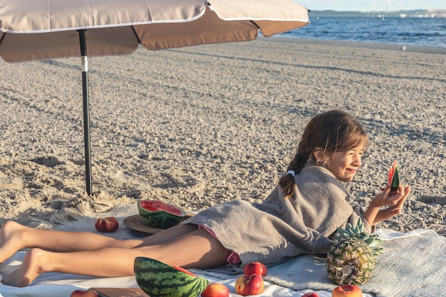 Niña come fruta sobre una manta en la playa