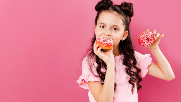 Niña comiendo deliciosas donas con espacio de copia