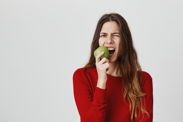 Niña comiendo manzana agria y haciendo muecas por el sabor