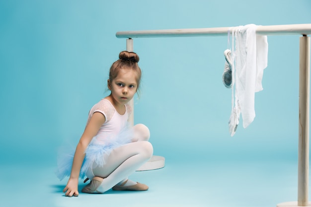 La niña como bailarina de balerina posando cerca del estante de ballet en estudio azul