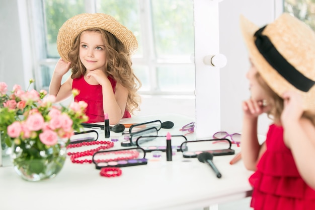 Foto gratuita una niña con cosméticos. ella está en el dormitorio de la madre, sentada cerca del espejo.