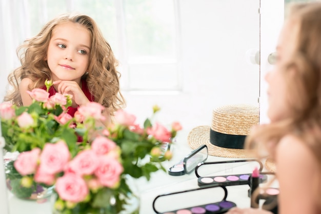 Una niña con cosméticos sentado cerca del espejo.