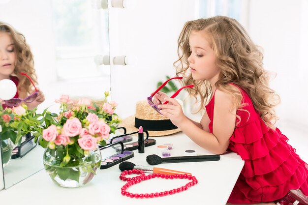 Una niña con cosméticos sentado cerca del espejo.