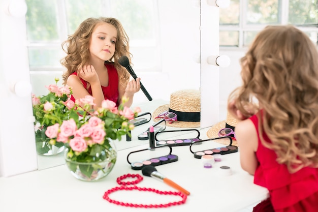 Una niña con cosméticos sentado cerca del espejo.