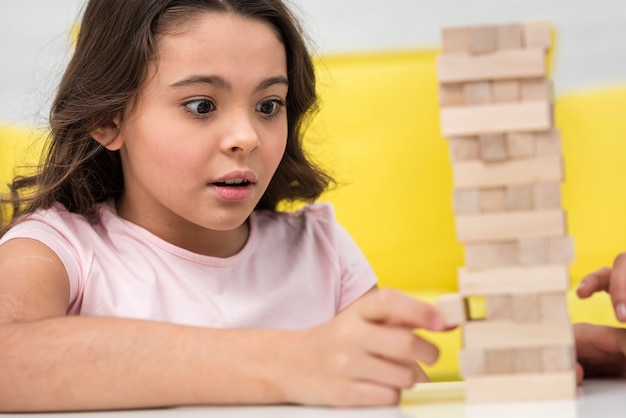 Foto gratuita niña cuidando al obtener una pieza de un juego de torre de madera