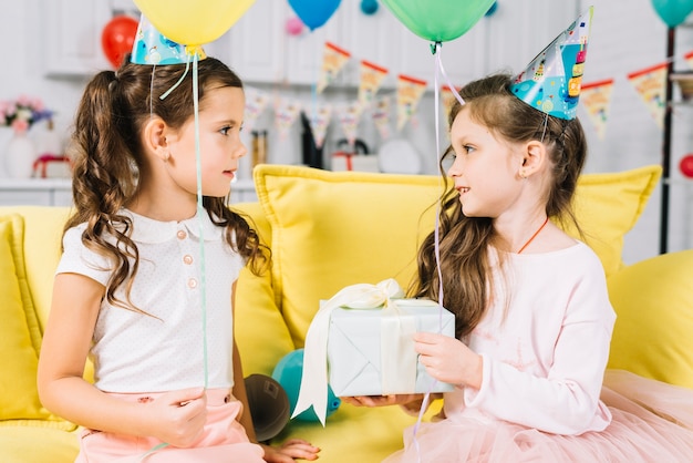 Niña de cumpleaños mirando a su amiga con regalos en mano en la fiesta de cumpleaños