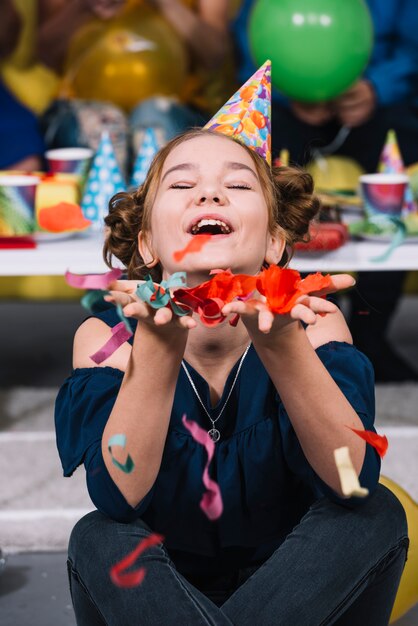 Una niña de cumpleaños con sombrero de fiesta en la cabeza con confeti cayendo en la mano