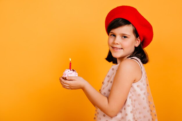 Niña de cumpleaños sonriente posando en boina francesa Foto de estudio de niño alegre con pastel aislado en amarillo