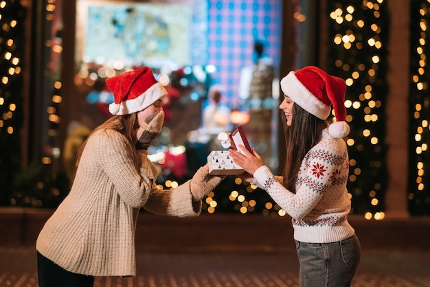 La niña le da un regalo a su amiga en la calle. Retrato de felices lindos jóvenes amigos