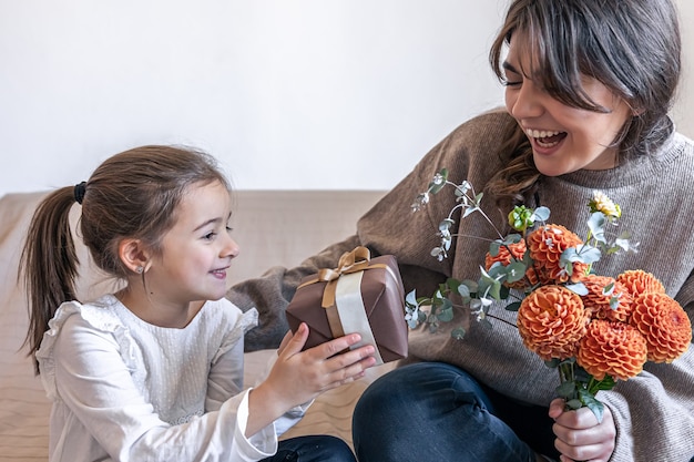 Una niña le da a su madre un regalo y un ramo de flores.