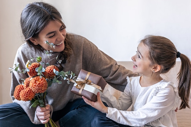 Una niña le da a su madre un regalo y un ramo de flores.