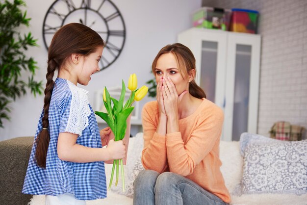 Niña dando a su mamá las flores y la tarjeta de felicitación.