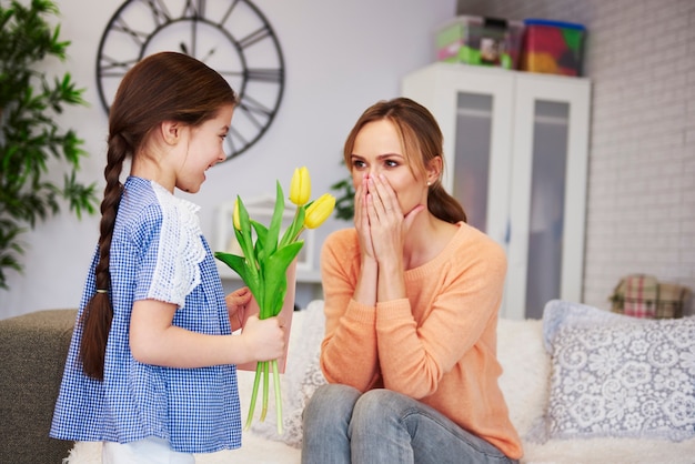 Niña dando a su mamá las flores y la tarjeta de felicitación.