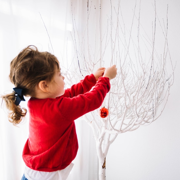 Foto gratuita niña decorando árbol blanco