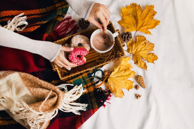 niña desayunando sabroso en la cama en bandeja de madera con taza de cacao, canela, galletas y donas glaseadas.