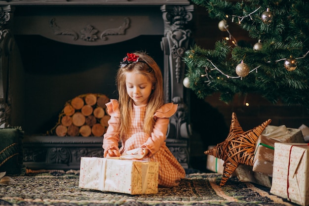 Niña desempaquetando regalos de navidad por arbol de navidad