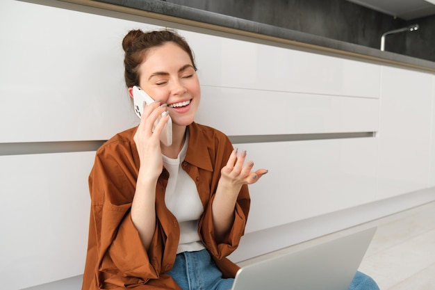 Foto gratuita niña despreocupada ríe habla por teléfono móvil llama a un amigo y tiene una conversación divertida sentada