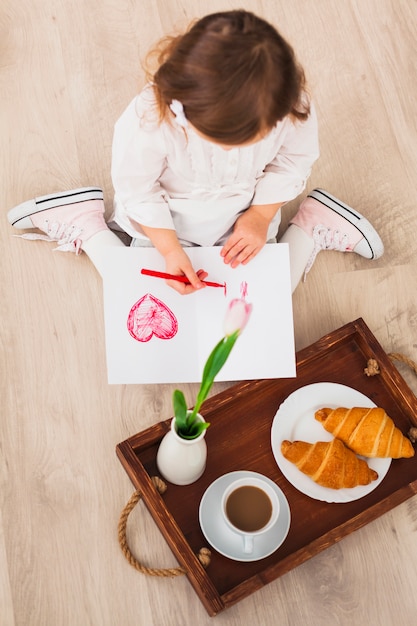 Foto gratuita niña dibujando corazón cerca de bandeja con café