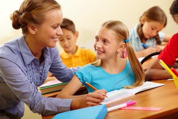 Niña dibujando con la maestra ayudando en clase