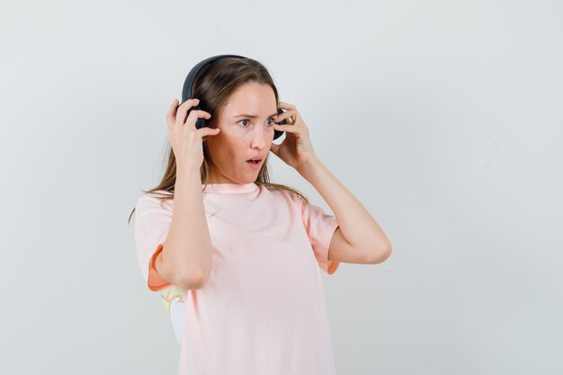 Niña disfrutando de la música con auriculares en camiseta rosa y mirando asombrado, vista frontal.