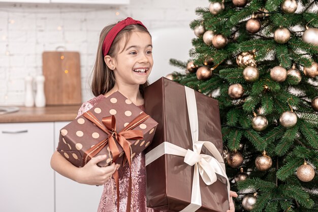 Niña divertida con cajas de regalo cerca del árbol de Navidad