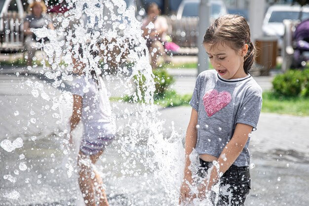 Niña divertida en una fuente, entre las salpicaduras de agua en un caluroso día de verano.