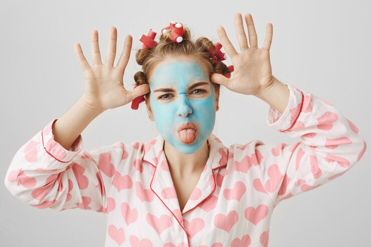 Foto gratuito niña divertida en rizadores de pelo y máscara facial mostrando lengua