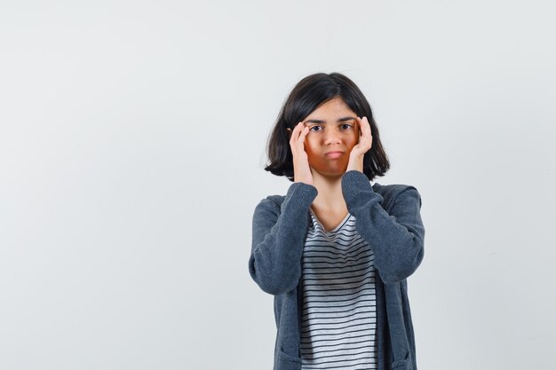 Niña con dolor de cabeza en camiseta, chaqueta y aspecto cansado.