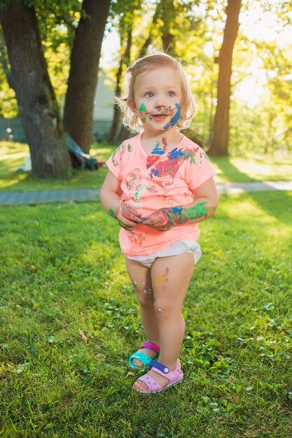 Niña de dos años manchada de colores contra el césped verde