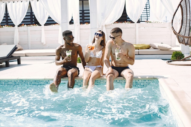 Niña y dos de sus amigos varones multirraciales relajándose en una tumbona cerca de la piscina