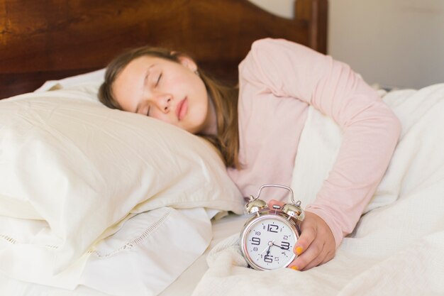 Niña durmiendo con despertador en la cama