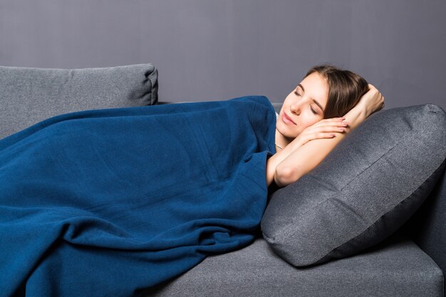 Niña durmiendo en un sofá cubierto con colcha azul sobre fondo gris