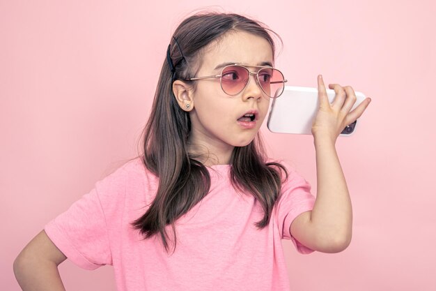 Niña elegante con un teléfono inteligente en un fondo rosa