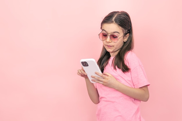 Niña elegante con un teléfono inteligente en un fondo rosa