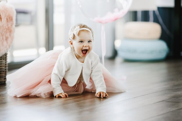 Niña en un encantador vestido rosa con la boca abierta se arrastra en el piso