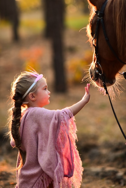 Foto gratuita niña encantadora vestida como una princesa se encuentra con un caballo en el bosque de otoño