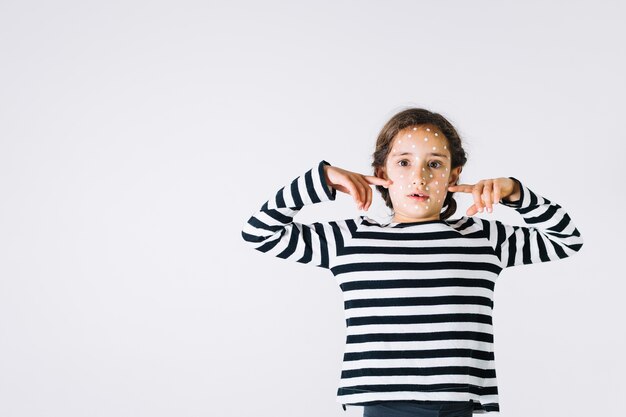 Niña enferma apuntando a las mejillas