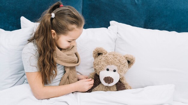 Niña enferma comprobando la temperatura del oso de peluche con termómetro