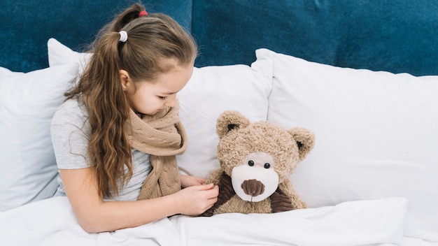 Niña enferma comprobando la temperatura del oso de peluche con termómetro