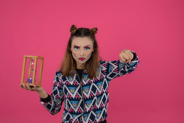 Niña enojada soldando maquillaje de fantasía y sosteniendo un reloj de arena. foto de alta calidad