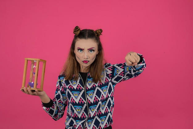 Niña enojada soldando maquillaje de fantasía y sosteniendo un reloj de arena. foto de alta calidad