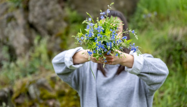 La niña esconde su rostro detrás de un ramo de flores frescas recogidas en el bosque