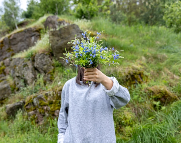 La niña esconde su rostro detrás de un ramo de flores frescas recogidas en el bosque