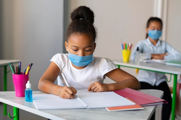 Niña escribiendo en clase mientras usa una máscara médica