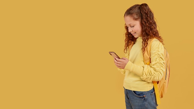 Niña de la escuela con camisa amarilla mirando el espacio de copia de teléfono